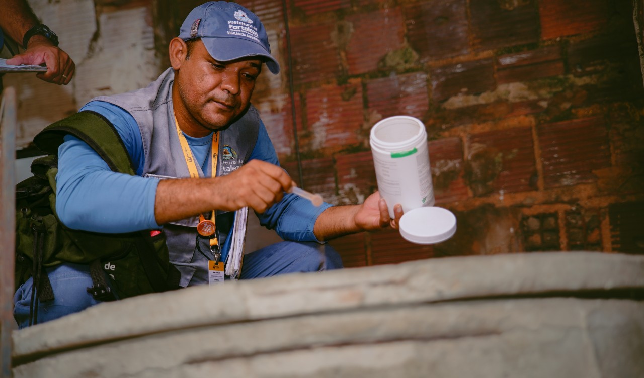 agente de endemia coloca pó em uma caixa d´água